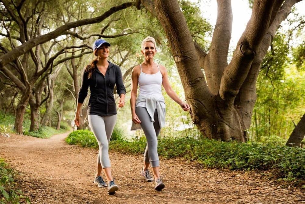 Dos mujeres caminando por un sendero de tierra entre árboles